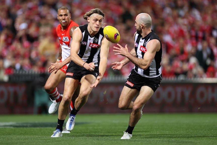 A Collingwood AFL player handballs to a teammate against Sydney.