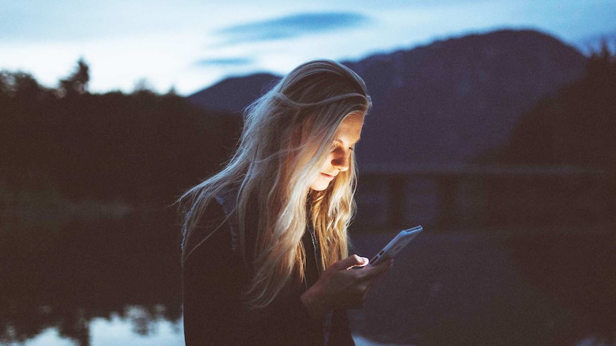 Young woman looks at her phone during the night to depict what to consider before announcing pregnancy or miscarriage online.