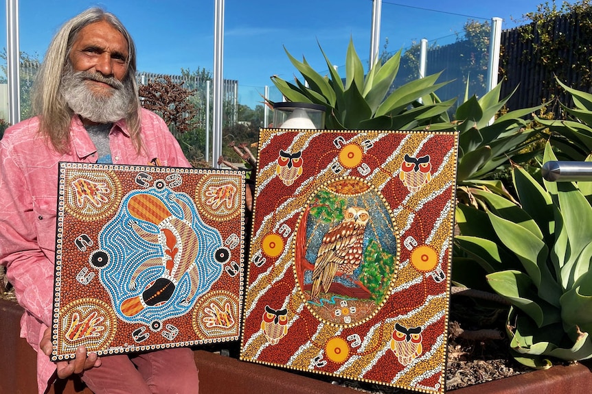 Stanley Geebung sits with two of his artworks outside in a garden.