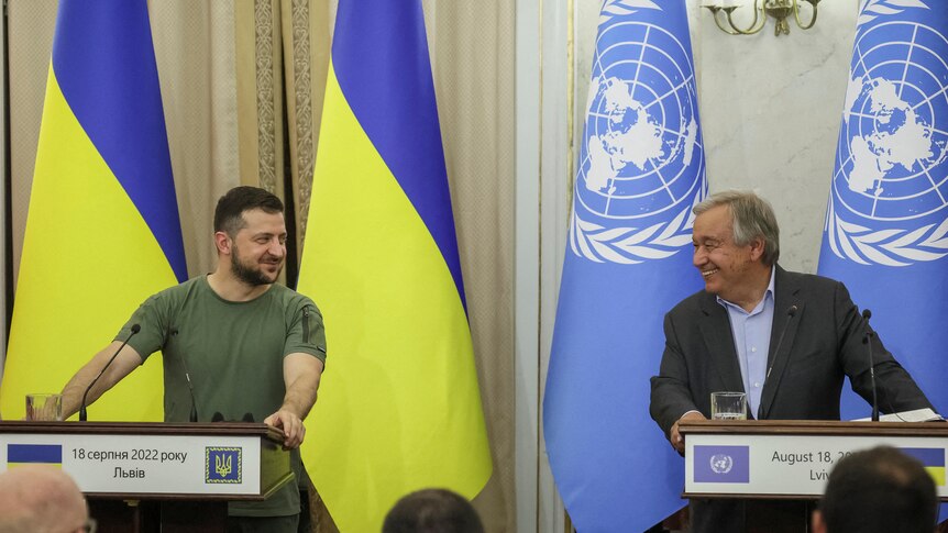 Zelenskyy and Antonio Guterres smile at each other from their podiums at a conference.