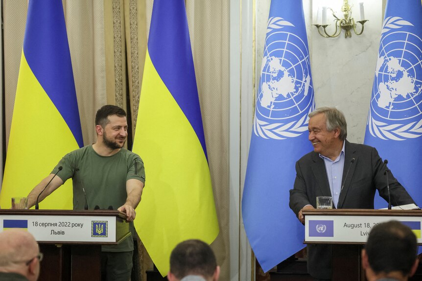 Zelenskyy and Antonio Guterres smile at each other from their podiums at a conference.