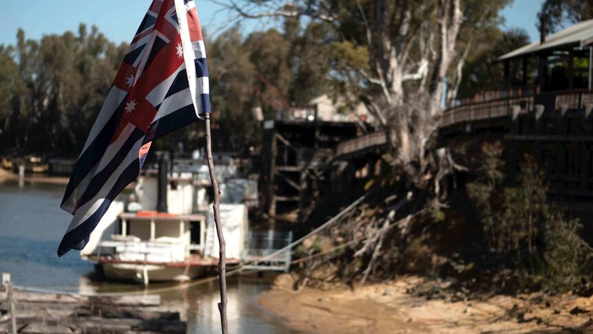 The flag of the Murray River is in focus, in the background the shores of murray river can be seen