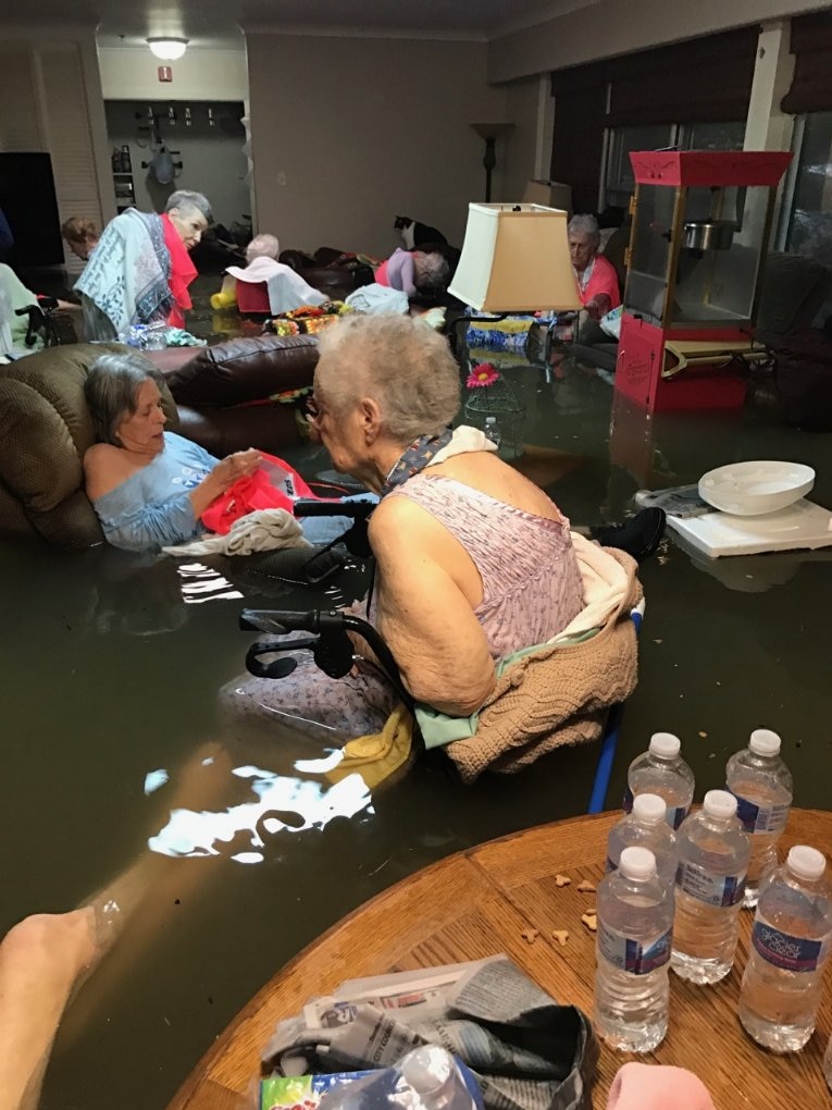 Nursing home residents sit in a room waist-deep in floodwaters