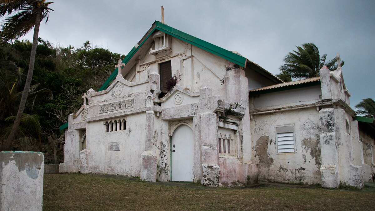 An old white church with green eaves. The paint is deterioriating.