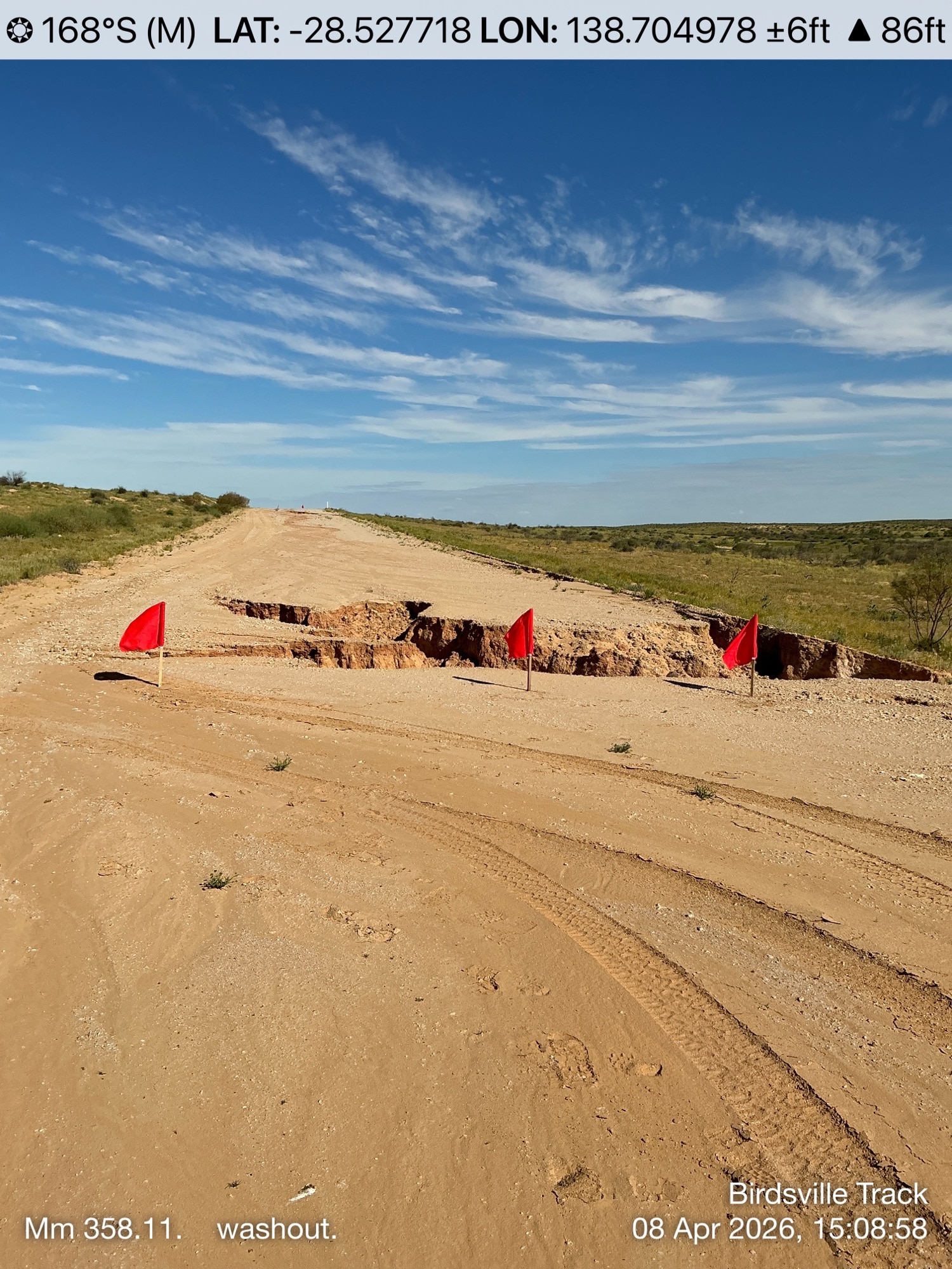A dirt road with a large chunk washed out, and flags marking the hole.