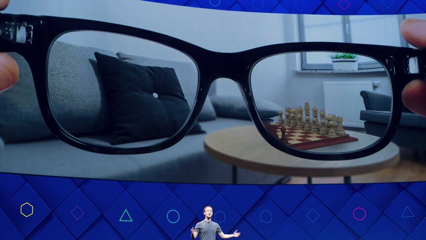 Mark Zuckerberg at F8 with augmented reality glasses on screen behind him