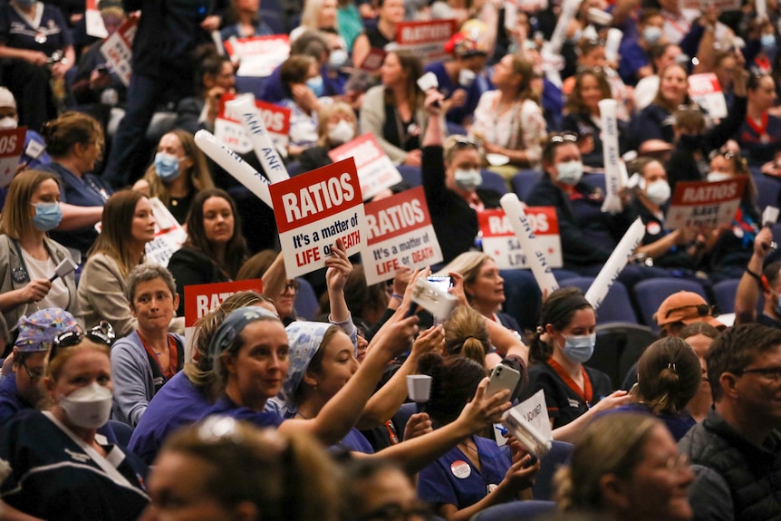 A tight shot of a crowd of nurses holding up signs calling for nurse-to-patient ratios