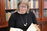State Library historian Anna Welch holds open a 200-year-old book with it open to a page with a cut picture cut out.