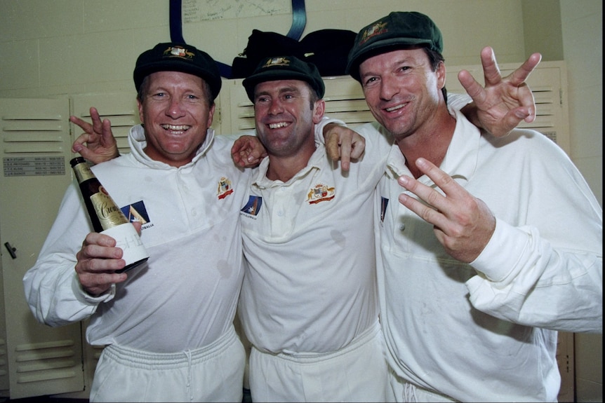 Three men in cricket whites smile at the camera