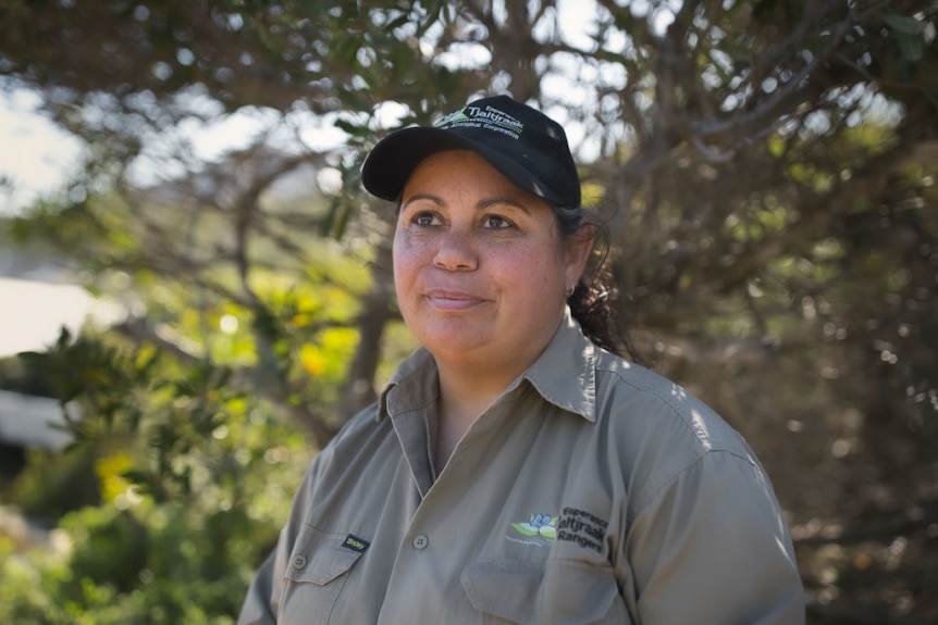 An Indigenous woman wearing a grey work shirt and a black cap.