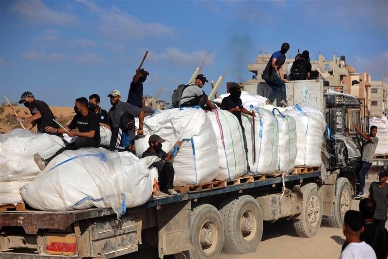 A large truck carrying sacks, with several people on the back armed with sticks.
