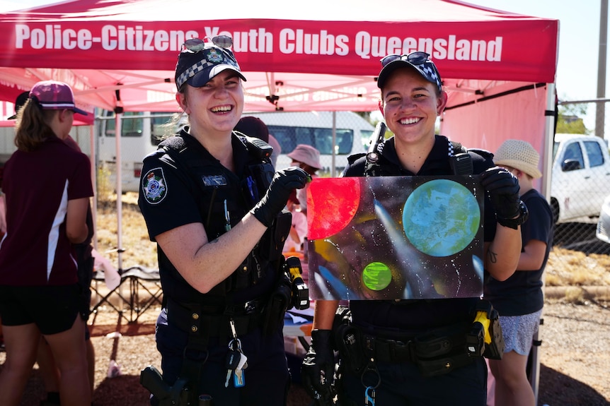 Two Queensland police officers (female) hold a spray painted piece of art.