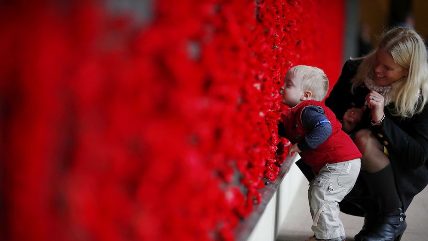 Naomi Laughton with 18-month-old Alexander Laughton place a poppy of the Roll of Honour after the Anzac Day dawn service