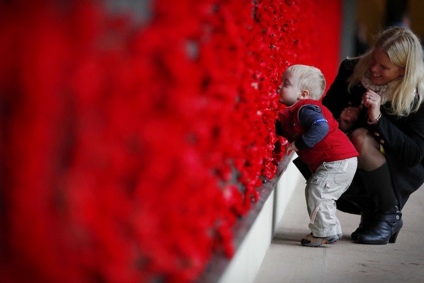 Naomi Laughton with 18-month-old Alexander Laughton place a poppy of the Roll of Honour after the Anzac Day dawn service