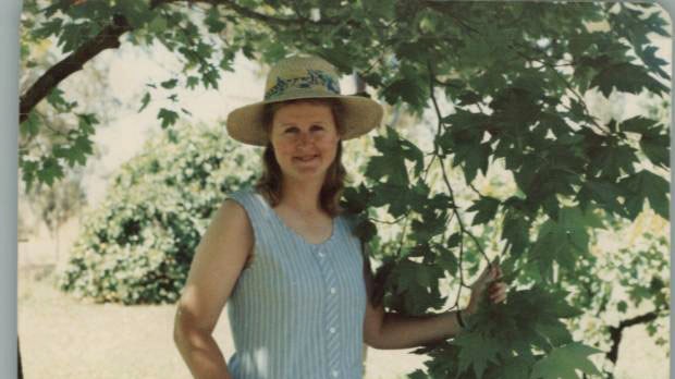 Penny Hill, wearing a hat and dress, stands under a tree.