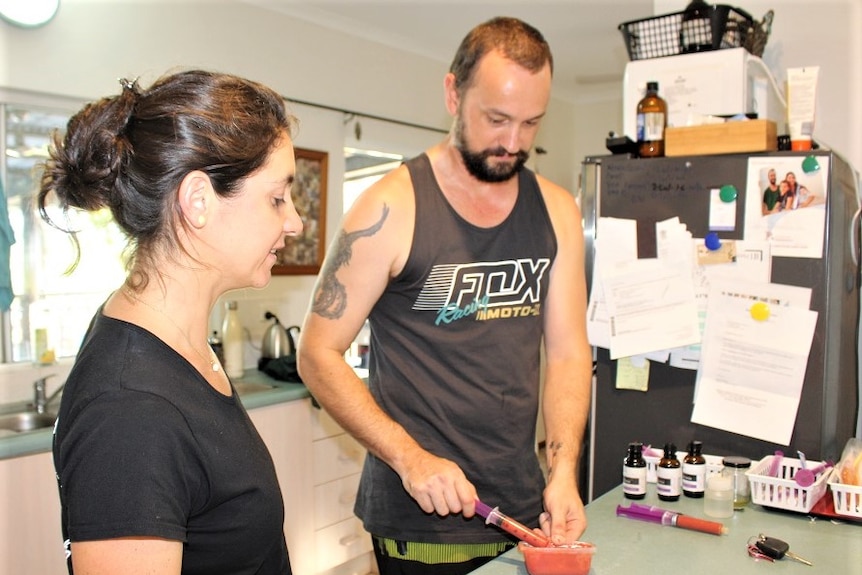 Young mother and father in kitchen putting healthy pink liquid into a syringe to feed to baby Enzo.