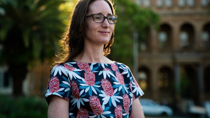 Dr Natasha Moore wears a floral t-shirt and glasses in a courtyard.