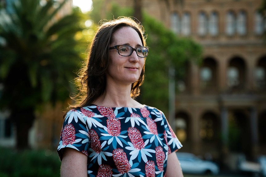 Dr Natasha Moore wears a floral t-shirt and glasses in a courtyard.