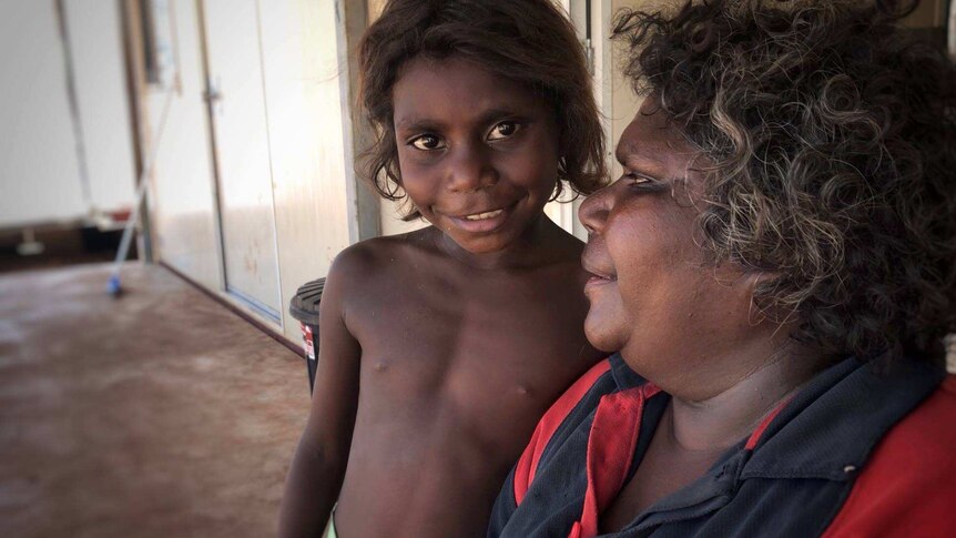 Young indigenous child smiling at camera while interpreter looks toward child.