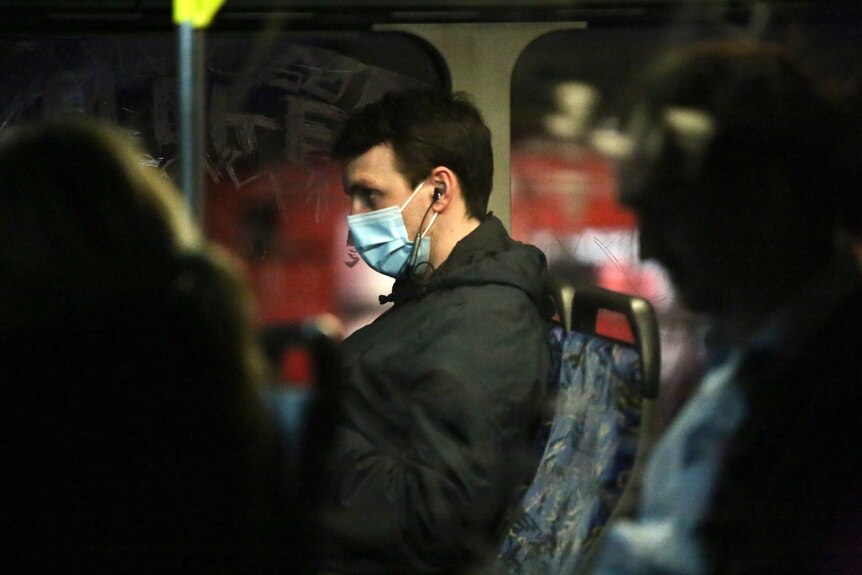 A man wears a face masks while sitting on a bus at night.