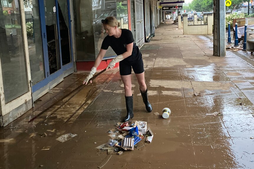 woman in black shirt and shorts sweeping a footpath