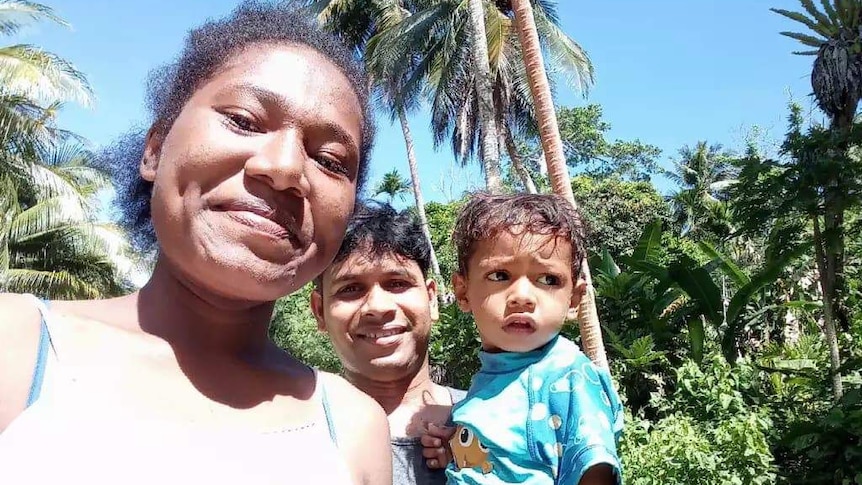 A smiling mother poses for a photograph with her husband who is holding their young son.