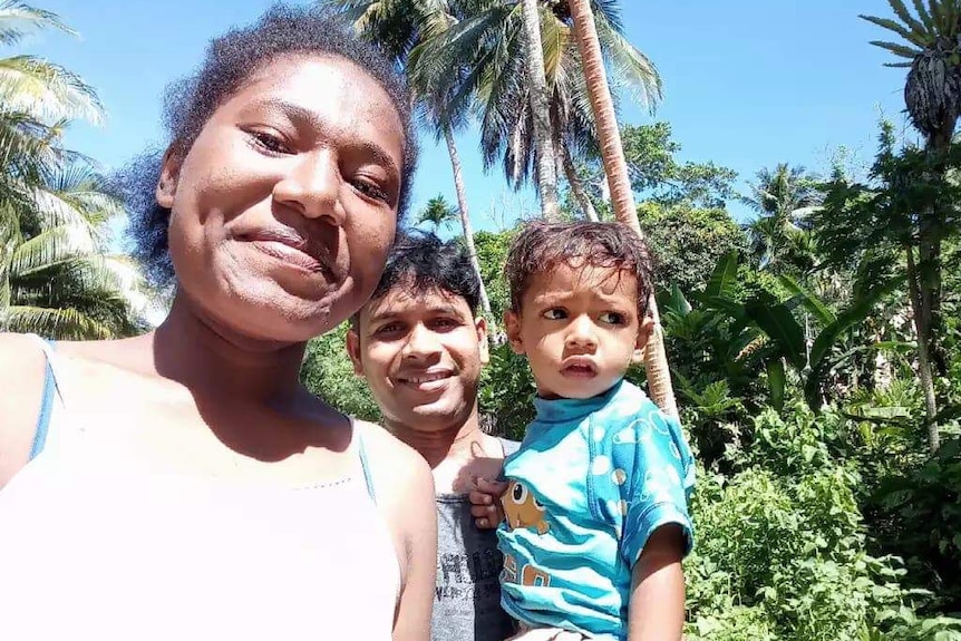 A smiling mother poses for a photograph with her husband who is holding their young son.