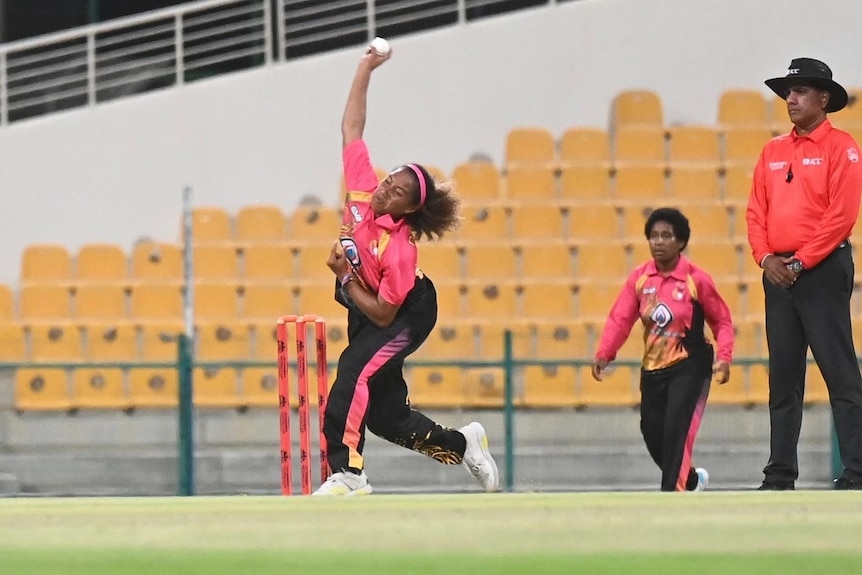 A female cricketer in long tracksuit pants and pink competition shirt about 