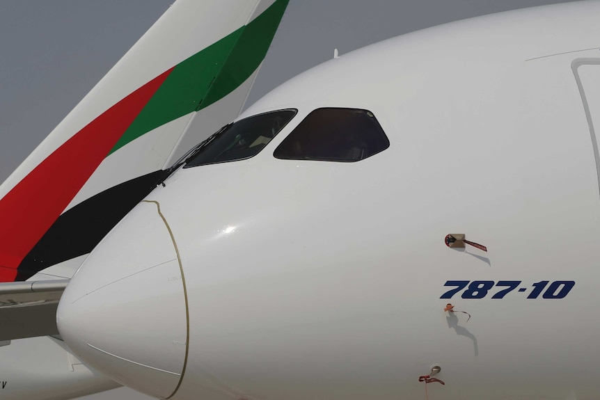 The nose of a Boeing 787-10 Dreamliner parked in front of an Emirates plane.