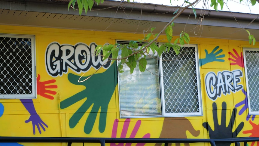 Outside of a yellow building with the words "grow" and "care" and colourful hands painted on