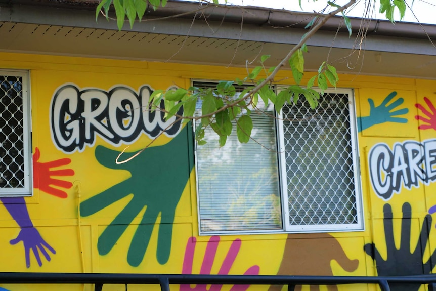 Outside of a yellow building with the words "grow" and "care" and colourful hands painted on