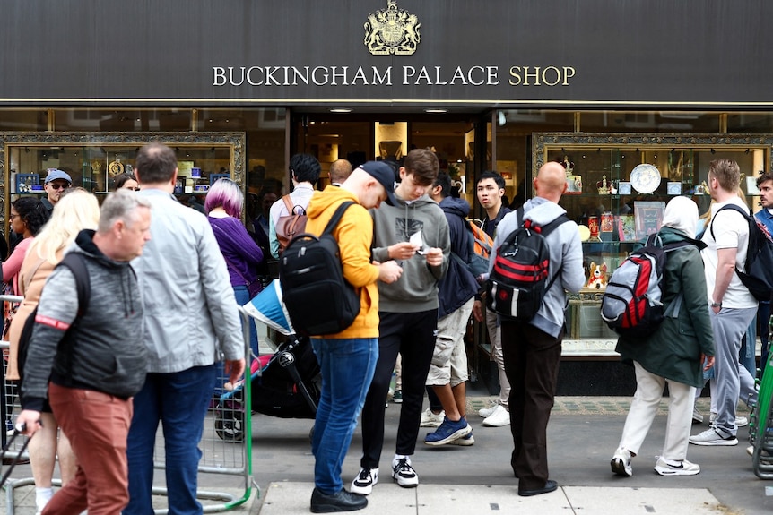 A large number of people outside a building that says Buckingham Palace Shop on it.