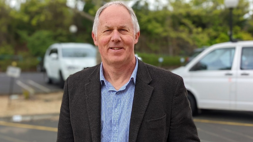 A grey-haired man stands in a car park with his hand in his pocket