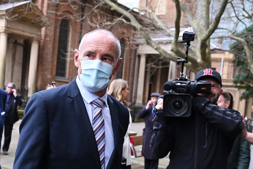 A man wearing a mask in front of a TV cameraman