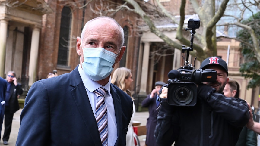 A man wearing a mask in front of a TV cameraman