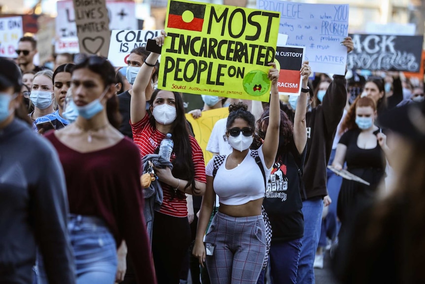 a group of people hold signs at the Black Lives Matter protest in Brisbane