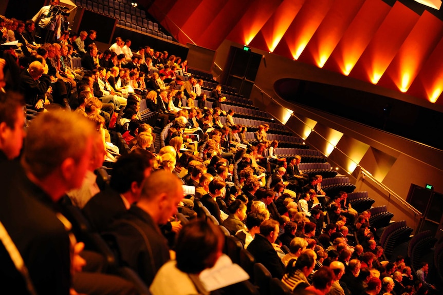 Around 100 people sit in the crowd in a theatre room at the Perth Convention Centre.