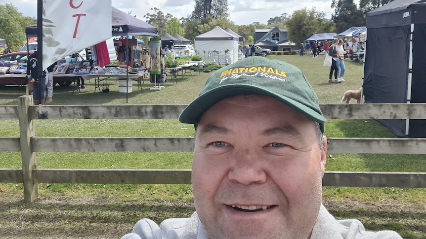 A selfie of a middle-aged man wearing a National party hat at a country market 