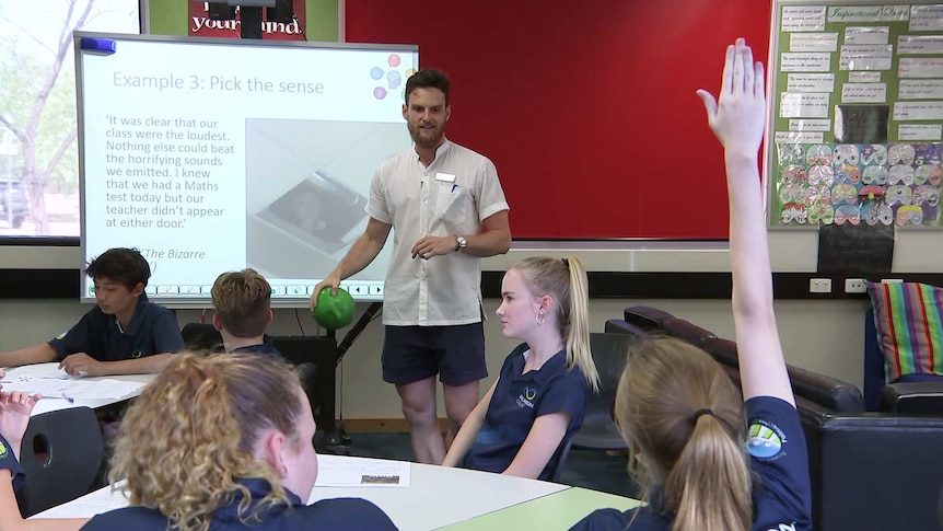 Michael Kingston stand by a whiteboard at the front of his class at Palmerston College while a student raises her hand.