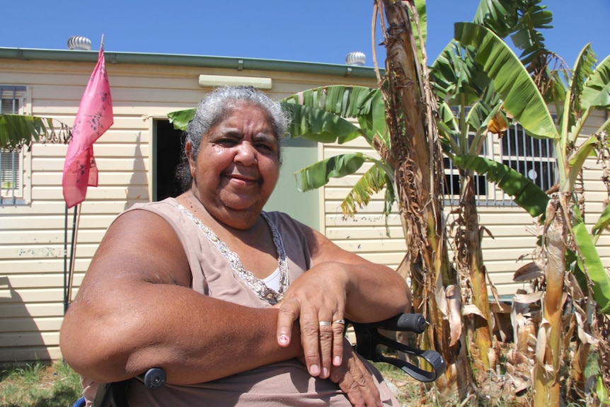 An Indigenous woman, Aunty Lorraine Brown, sits in front of the historic Coomaditchie community hall.