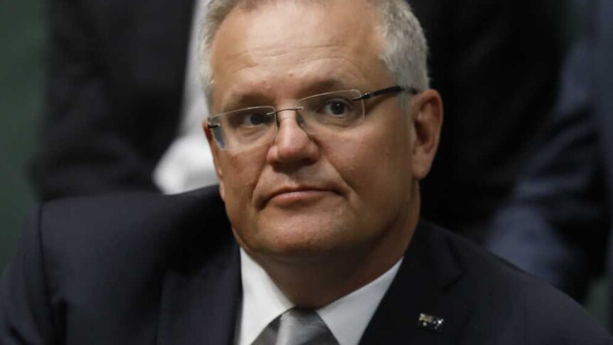Scott Morrison sitting and looking off to the right, wearing a dark suit, white shirt and silver tie.