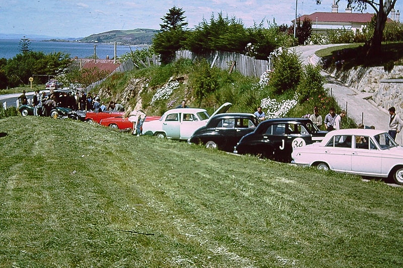 A row of cars in a residential laneway, being worked on ahead of the race