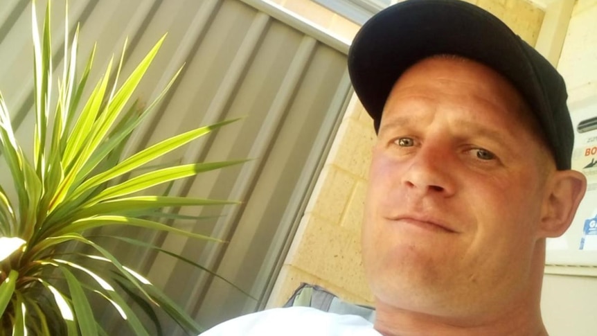 A close up photo of a man wearing a black cap and a white t-shirt.