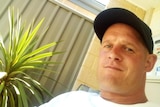 A close up photo of a man wearing a black cap and a white t-shirt.