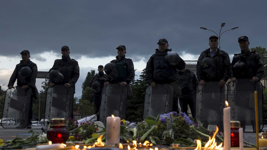 Macedonian police stand in front of a memorial for the victims of a gun battle in Kumanovo