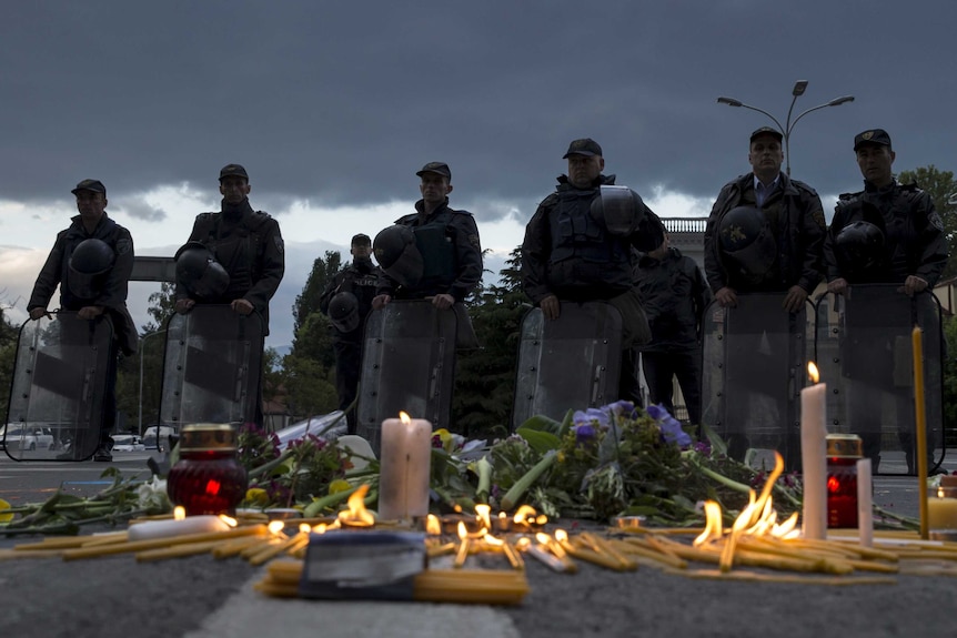 Macedonian police stand in front of a memorial for the victims of a gun battle in Kumanovo