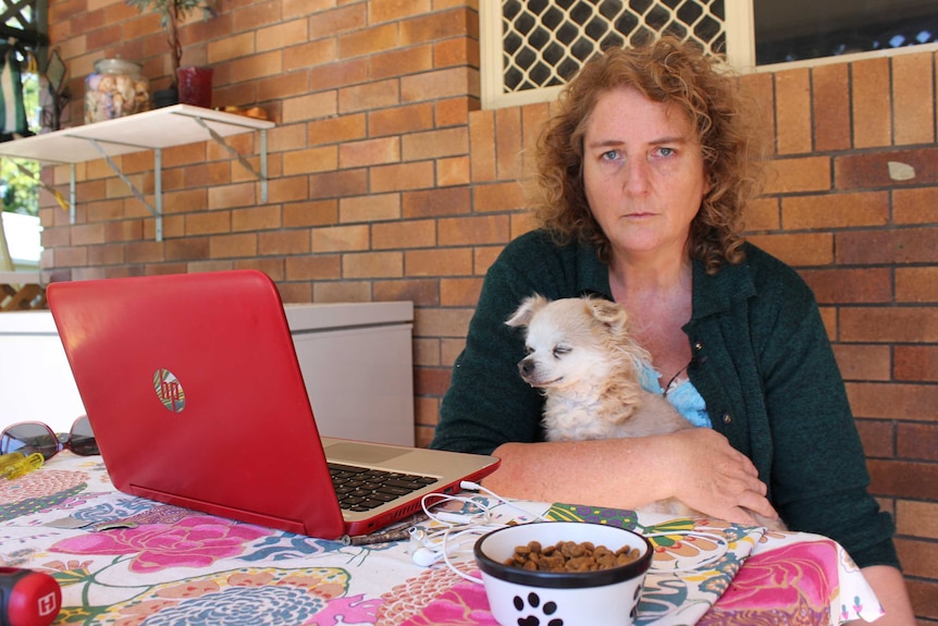 Nichola Ryan sits at a table with a dog on her lap