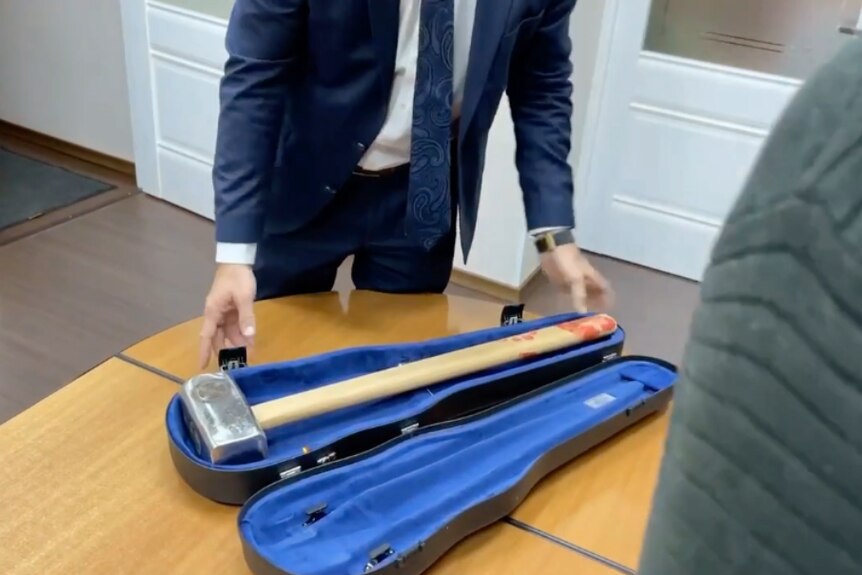 A large sledgehammer in a violin case on a table.
