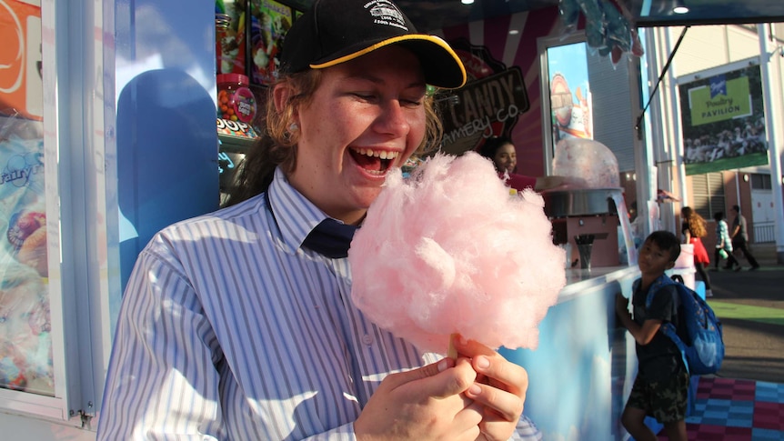 A girl smiles as she looks at a large stick of pink fairy floss.