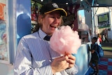 A girl smiles as she looks at a large stick of pink fairy floss.